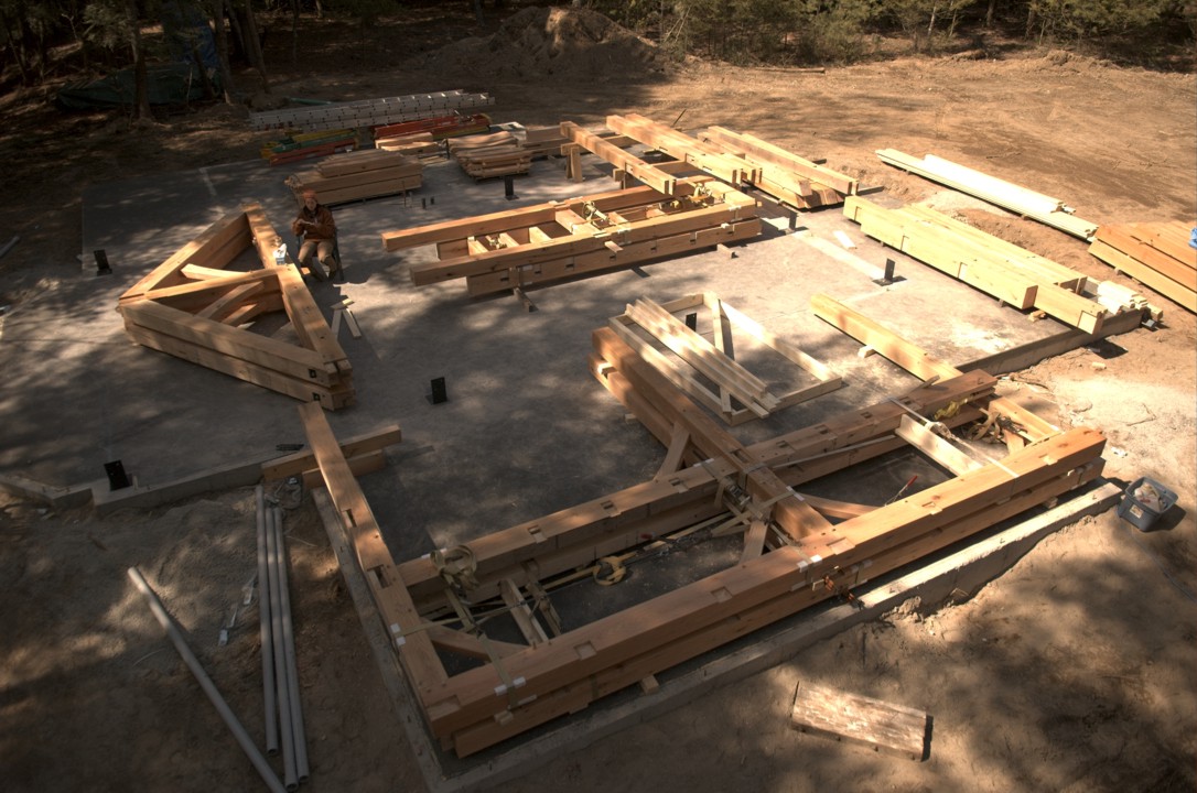 The timber frame is partially built on the ground prior to the raising; Lucie sits in the middle